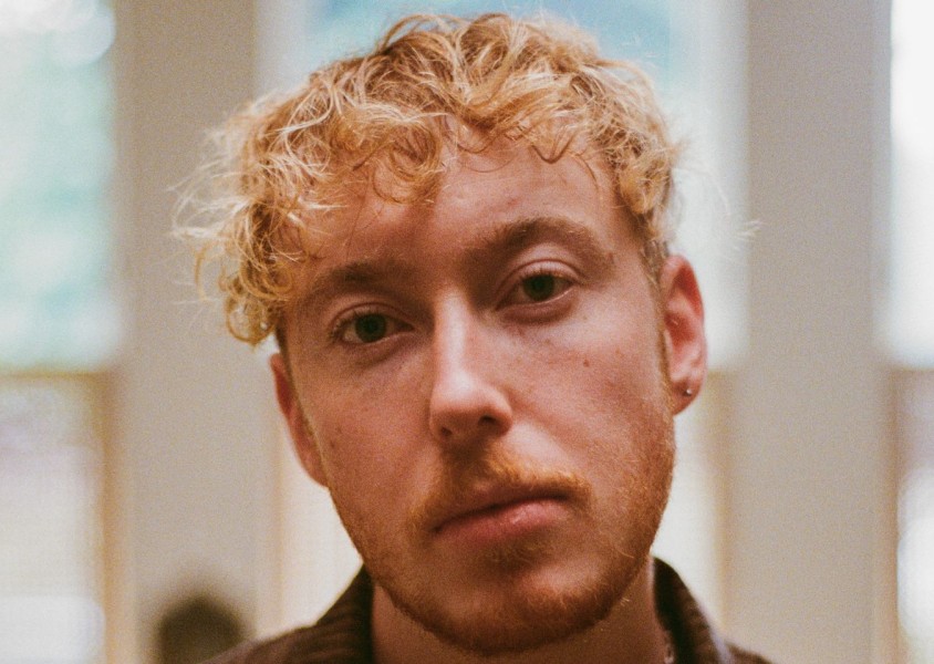 A close up image of a person with blonde curly hair and one ear piercingx